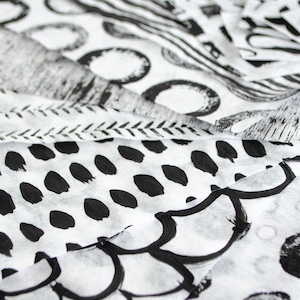May include: Close-up of white fabric with various black patterns. The designs include organic shapes, dots, and lines, creating a layered effect. The fabric appears to be thin and possibly used for crafting or design projects.