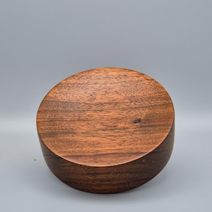 Peut inclure: Un bol en bois artisanal de couleur brun foncé. Le bol a une forme arrondie avec une base plate et une surface lisse et polie. Le grain du bois est visible, ce qui ajoute à son esthétique naturelle. Idéal pour la décoration.