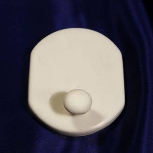May include: A white plastic hook with a round knob. The hook is mounted on a white plastic base.