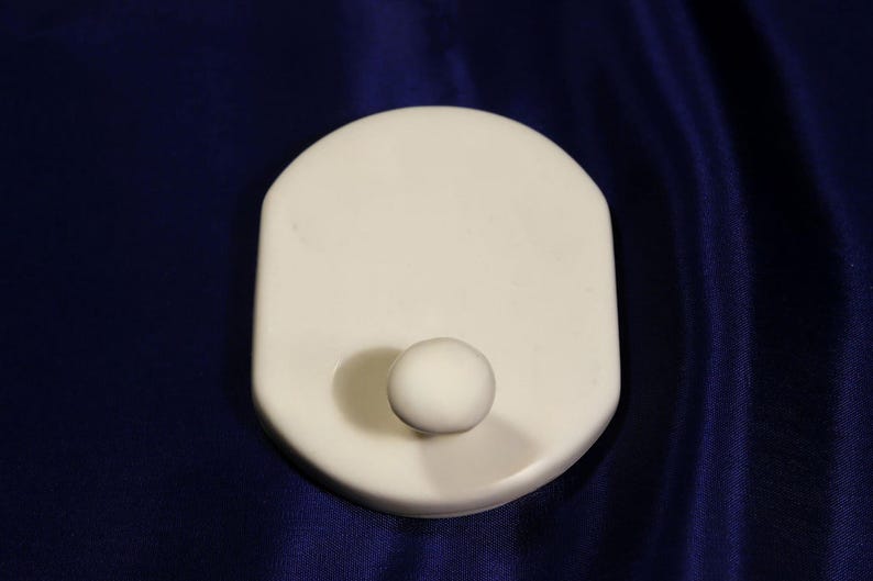 May include: A white plastic hook with a round knob. The hook is mounted on a white plastic base.