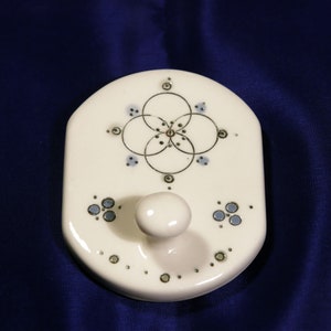 May include: White ceramic wall hook with a blue and gold geometric design. The hook has a rounded knob.