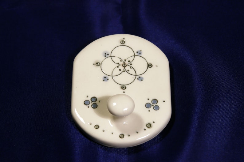 May include: White ceramic wall hook with a blue and gold geometric design. The hook has a rounded knob.