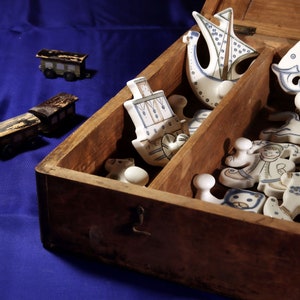 Könnte beinhalten: Eine Holzkiste mit einem Scharnierdeckel, gefüllt mit Keramikfiguren. Die Figuren sind in Blau und Weiß mit einem nautischen Thema bemalt. Die Kiste steht auf einer blauen Oberfläche.