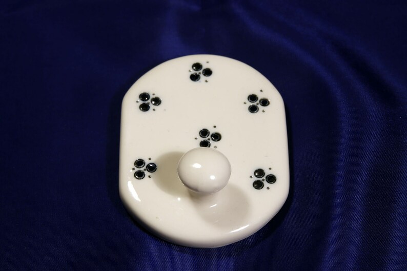 May include: White ceramic hook with a single hook and five black floral designs.