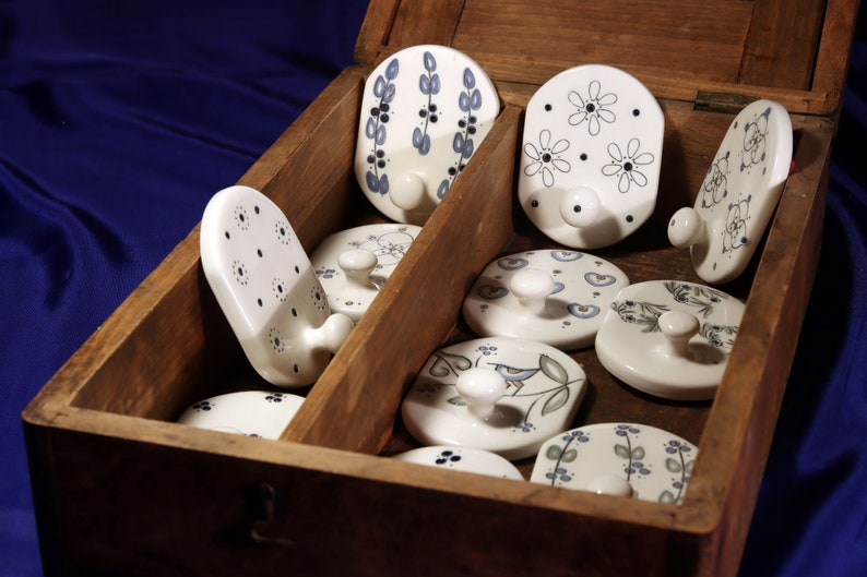 May include: A wooden box filled with ceramic hooks with various blue and white floral designs. The hooks are all white with a blue floral pattern and a white hook.