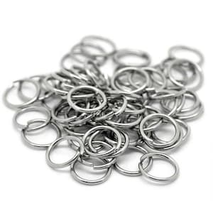 May include: A pile of small, shiny, silver-colored metal split rings. These open rings are circular and have a split, allowing them to be opened and closed. They are likely used for attaching items like keys or charms.