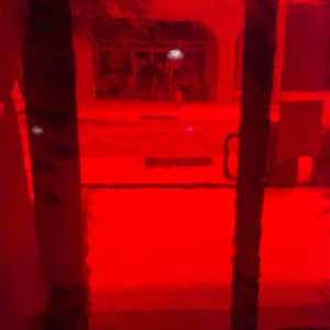 Könnte beinhalten: Ein rot getöntes Bild eines Türrahmens und einer Straßenszene. Das Bild wird von einem tiefroten Farbton dominiert, wobei die Tür und die Straßendetails durch den roten Filter sichtbar sind. Der Türgriff ist sichtbar.