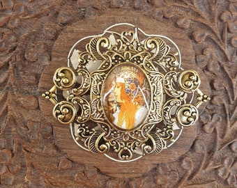 grote goudkleurige broche met een afbeelding van een plaat van Alphonse Mucha