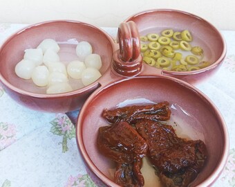 May include: A three-sectioned serving dish with a brown glaze. The dish contains white onions, green olives, and sun-dried tomatoes.