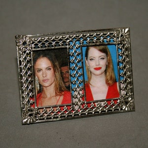 Op de afbeelding: Een zilveren fotolijst met twee foto's van vrouwen. De lijst heeft een decoratief ontwerp en de foto's zijn in kleur.