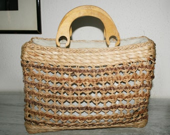 May include: A woven straw handbag in natural brown and tan tones. The bag features a woven design and two wooden handles.