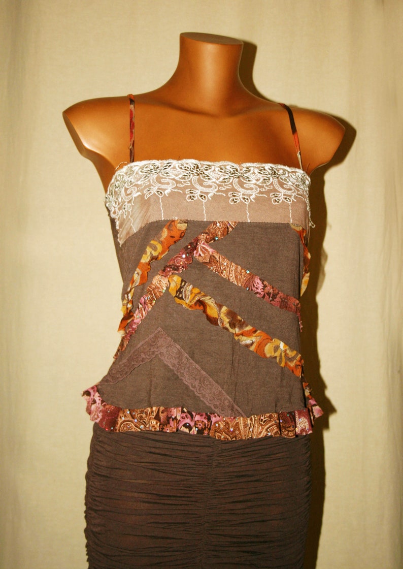 May include: A brown sleeveless top with a lace trim and layered fabric details. The top has a ruffled hem and a brown skirt.