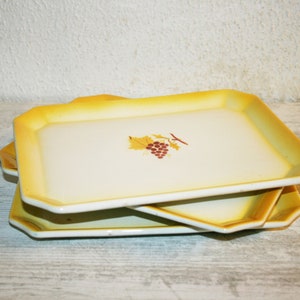 May include: Three yellow ceramic serving trays with a grape design. The trays are stacked on top of each other.