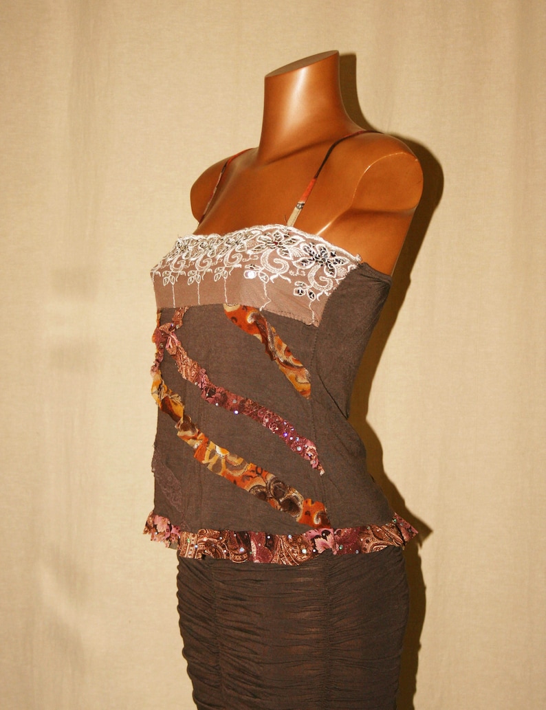 May include: A brown sleeveless top with a white lace trim and brown and orange patterned fabric accents. The top has a fitted bodice and a flowing skirt.