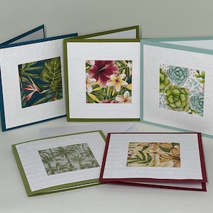 May include: Five blank greeting cards with different floral patterns. The cards are all white with a textured surface and have a colored border. The floral patterns include tropical leaves, a hibiscus flower, and succulents.