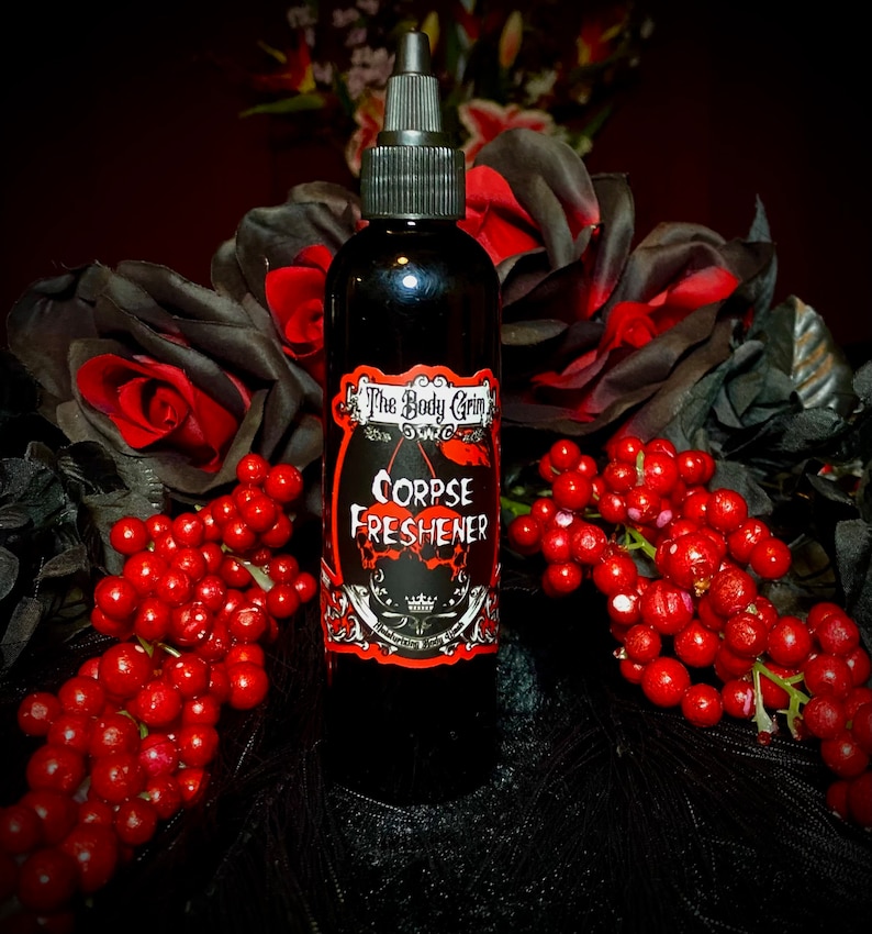 May include: A black glass bottle with a black label that says "The Body Grim Corpse Freshener". The bottle is surrounded by red berries and black flowers.