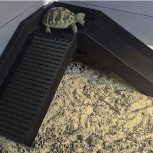 May include: A black L-shaped ramp with a textured, slatted surface for traction, featuring a small tortoise walking on the top platform. The text FOR BABY TORTS is printed in light blue on the left side of the image, above the ramp structure.