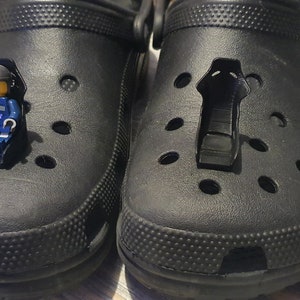 May include: A pair of black rubber clogs with a small blue and black Lego figurine sitting in one of the clogs.