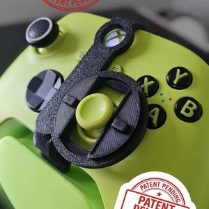 May include: A lime green video game controller with black buttons and a black attachment. The controller has the letters X, Y, A, and B in yellow. The text "PATENT PENDING" is stamped on the controller.