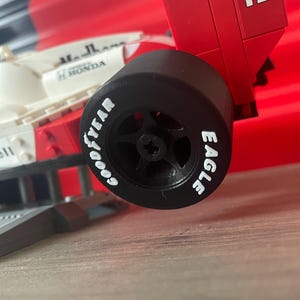 K&ouml;nnte beinhalten: Ein schwarzer Reifen mit wei&szlig;er Beschriftung "GOODYEAR EAGLE" auf einem roten und wei&szlig;en Spielzeug-Rennwagen mit der Nummer 12 auf der R&uuml;ckseite.