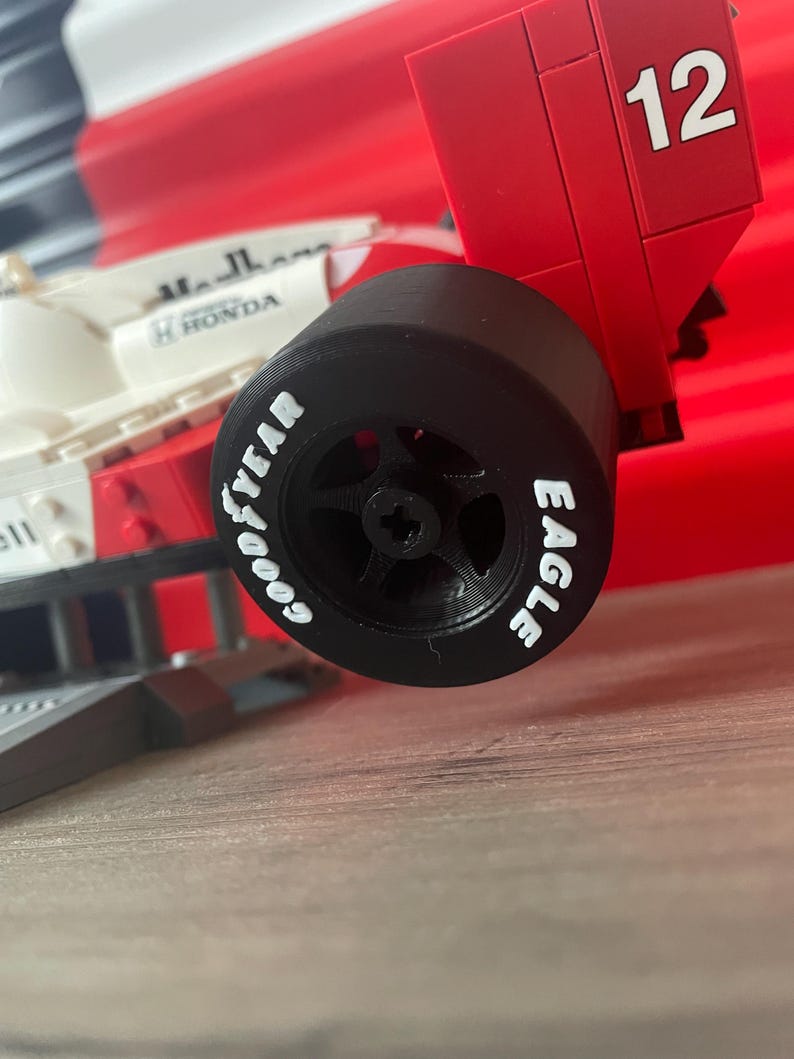 K&ouml;nnte beinhalten: Ein schwarzer Reifen mit wei&szlig;er Beschriftung "GOODYEAR EAGLE" auf einem roten und wei&szlig;en Spielzeug-Rennwagen mit der Nummer 12 auf der R&uuml;ckseite.