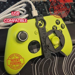 May include: A lime green Xbox controller with a black attachment and a white USB cable. The controller has black buttons and the text "USB COMPATIBLE". The image also includes a "Patent Pending" stamp.