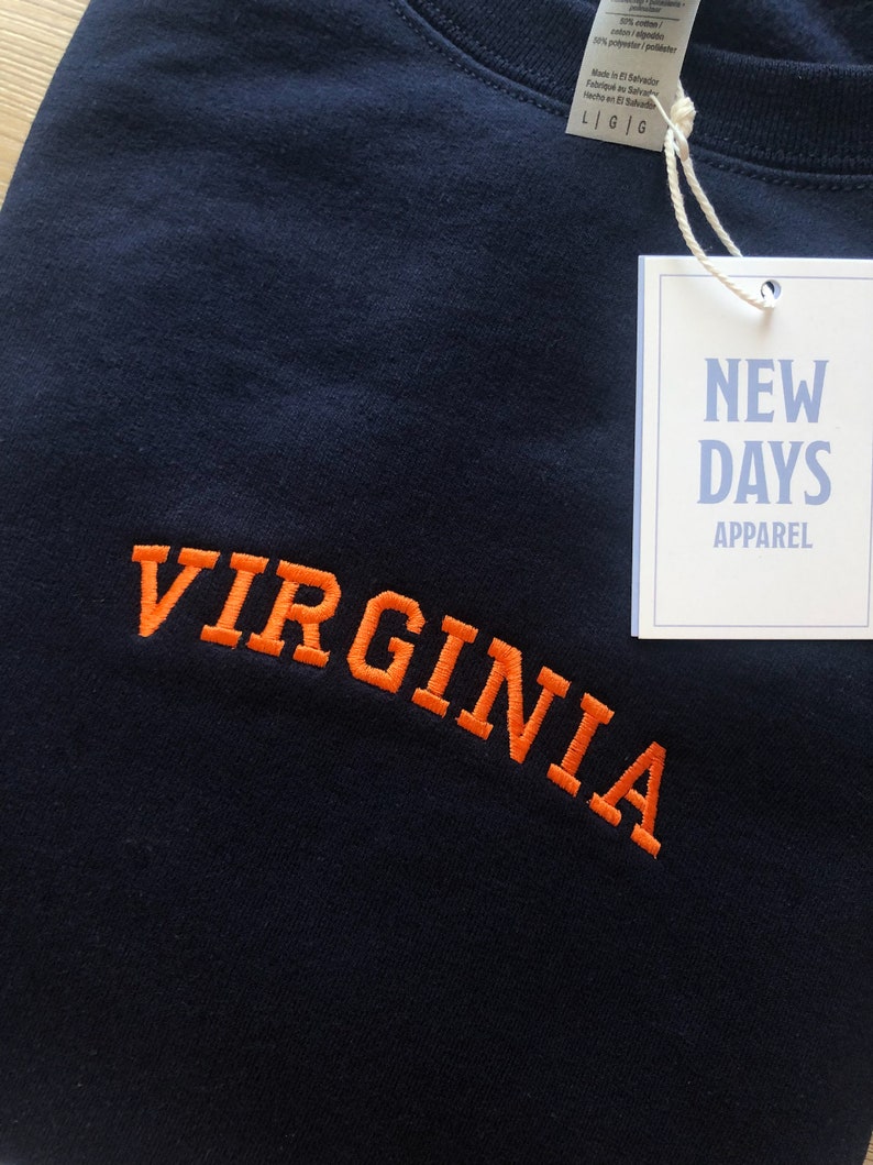 May include: A navy blue t-shirt with the word "VIRGINIA" embroidered in orange. The shirt has a tag attached that says "NEW DAYS APPAREL".