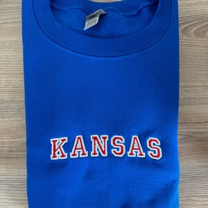 May include: A royal blue sweatshirt with the word "KANSAS" embroidered in red with white outlines.