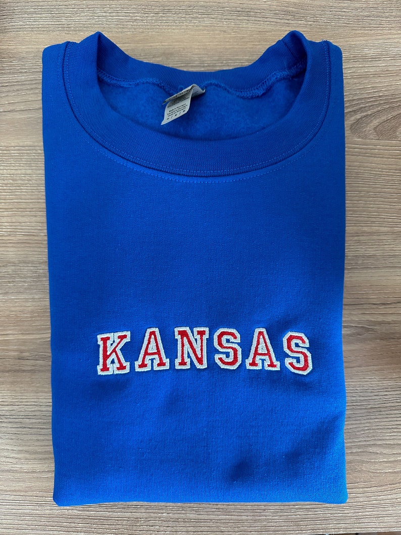 May include: A royal blue sweatshirt with the word "KANSAS" embroidered in red with white outlines.