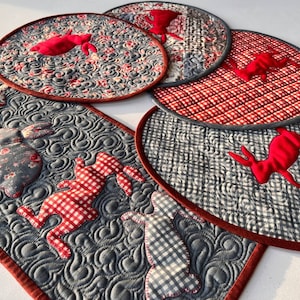 May include: Set of five quilted placemats featuring a red and white gingham pattern and a red bunny design. The placemats are made of a gray fabric with a quilted pattern.