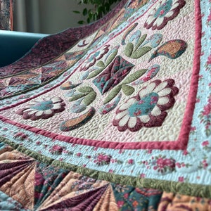 Può includere: Una trapunta con un motivo floreale rosa, verde e marrone. La trapunta è realizzata con quadrati di tessuto cuciti insieme e ha una texture trapuntata.