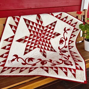 Może przedstawiać: Biała i czerwona kołdra z dużym wzorem gwiazdy w środku. Kołdra leży na drewnianej ławce z doniczką z rośliną w tle.