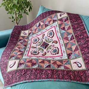 May include: A pink and green quilt with a floral design in the center. The quilt is made with a variety of fabrics and has a quilted pattern.