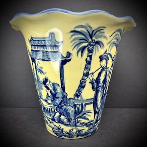 May include: A yellow ceramic vase with a scalloped rim and blue and white hand-painted Asian-inspired design. The vase features two figures, a palm tree, and a pagoda.
