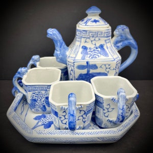 May include: A blue and white porcelain tea set with a teapot, four cups, and a tray. The teapot has a lid with a star design and the cups have handles shaped like dragons. The tray has a geometric pattern.
