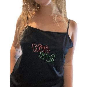 May include: Black camisole with thin straps featuring the embroidered text "WUB WUB" in neon pink and green. The top is made of a smooth, dark fabric.