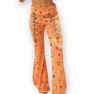 May include: Orange and white flared pants with a floral pattern and lace-up detailing on the sides. The pants have gold buttons on the lace-up detailing.