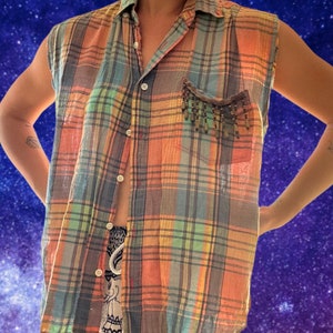 May include: A sleeveless plaid button-up shirt with a beaded pocket detail. The shirt is made from a lightweight fabric and has a relaxed fit.