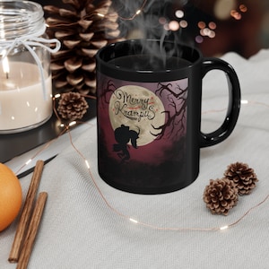 May include: Black coffee mug with a white silhouette of a creature with a red hat and a red knife. The mug has the text "Merry Krampus" in red and white on a purple background with a full moon and trees.
