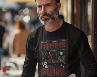 May include: Black long-sleeve shirt with a festive Krampus design. The design features the text "KRAMPUS IS COMING" in a pixelated font, along with a Krampus illustration and holiday accents. The shirt is worn by a person.
