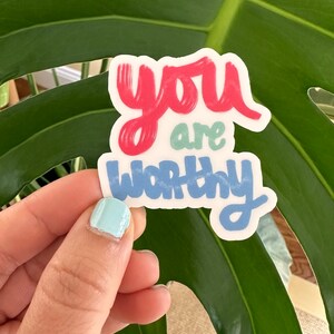 Puede incluir: Una pegatina con las palabras "you are worthy" en una fuente manuscrita colorida. Las palabras "you" y "worthy" están en azul, y "are" está en verde.