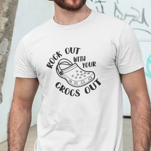 Könnte beinhalten: Weißes T-Shirt mit einer schwarzen Grafik eines Crocs-Schuhs und dem Text "Rock Out With Your Crocs Out".