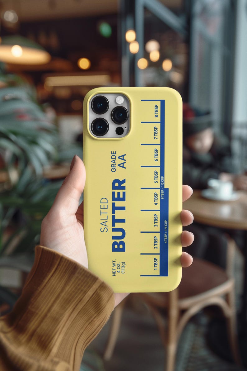 May include: A yellow phone case featuring a design inspired by a stick of butter. The case has the words "SALTED BUTTER AA" in blue, with measurement markings in tablespoons and cups. The net weight is 4 oz (113g).