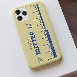 May include: A light yellow phone case with a blue butter measuring guide printed on it. The text "SALTED BUTTER AA GRADE" is printed in blue. The case has a measurement guide with tablespoon increments and a net weight of 4 oz (113g).