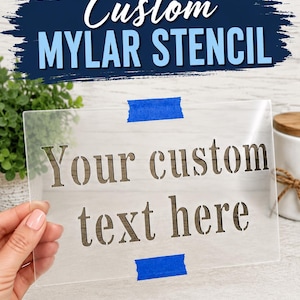May include: A clear rectangular Mylar stencil featuring the laser-cut text "Your custom text here" in a serif font. The stencil is secured with two strips of blue painter's tape. The text "Custom MYLAR STENCIL" appears in large blue letters above.