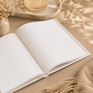May include: An open notebook with white pages featuring thin, horizontal gray lines. The notebook is positioned on a flat surface, displaying two blank, lined pages ready for writing. The paper is clean and bright, providing a clear space for notes.