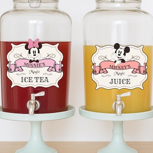 May include: Two large glass beverage dispensers, one filled with red liquid labelled "Minnie's Magic Ice Tea" and the other with yellow liquid labelled "Mickey's Magic Juice". Both dispensers sit on light blue pedestals. Additional bottles and straws are also visible.