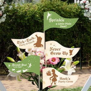 May include: A display of floral decorations with themed flags. The flags, in green and cream, display phrases like "Sprinkle a Little Pixie Dust!" and "Never Grow Up", along with illustrations. The arrangement is set against a backdrop of greenery and flowers.