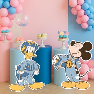 Peut inclure: Scène de fête avec des découpes de Donald Duck et Mickey Mouse en combinaisons spatiales bleues. Ballons roses et bleus, petits gâteaux et un chiffre 5 lumineux créent une ambiance festive.