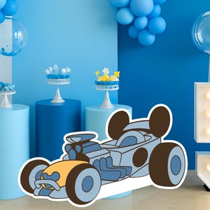 Può includere: Un'auto da corsa a fumetti blu e gialla con orecchie di Topolino è il punto focale di una scena di festa. Palloncini blu e alzatine per torte con dolcetti sono disposti su piedistalli blu. Un grande numero 5 illuminato è sulla destra.